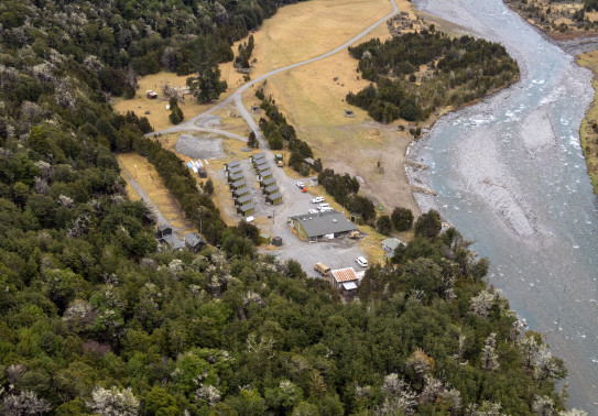 An aerial view of Dip Flat. This camp consists of one large building, 14 cabins and four other smaller buildings. The camp is located next to a river on the right and otherwise is surrounded by trees.