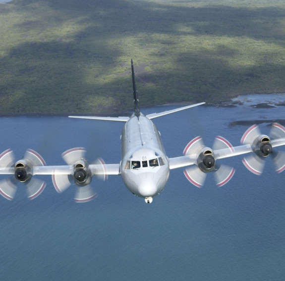 P-3K2 Orion flies over the ocean with land behind it. 