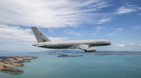 A Royal New Zealand Air Force Boeing 757-2K2 aircraft flies over the ocean but in the frame you can also see parts of land.