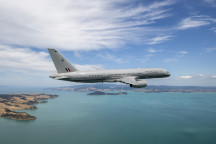 A Royal New Zealand Air Force Boeing 757-2K2 aircraft flies over the ocean but in the frame you can also see parts of land.