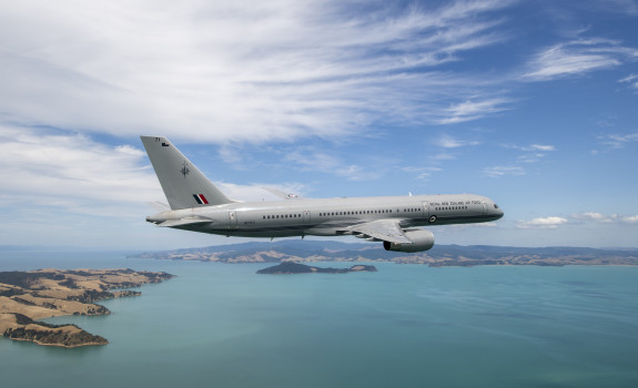 A Royal New Zealand Air Force Boeing 757-2K2 aircraft flies over the ocean but in the frame you can also see parts of land.