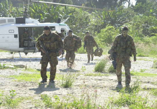 Four uniformed soldiers walk toward the camera after getting off a helicopter in a clearing within a jungle.