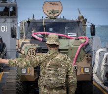 A NZ Army soldier guides an Australian armoured Bushmaster vehicle onto the beach at Cowley Beach
