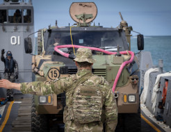 A NZ Army soldier guides an Australian armoured Bushmaster vehicle onto the beach at Cowley Beach