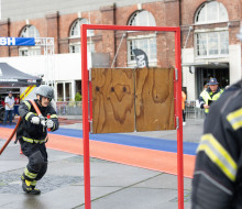 A firefighter with a red hose pipe over his shoulders runs towards a wooden shutter door on a red metal frame during the Firefighter Challenge in Wellington.