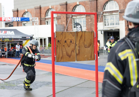 A firefighter with a red hose pipe over his shoulders runs towards a wooden shutter door on a red metal frame during the Firefighter Challenge in Wellington.