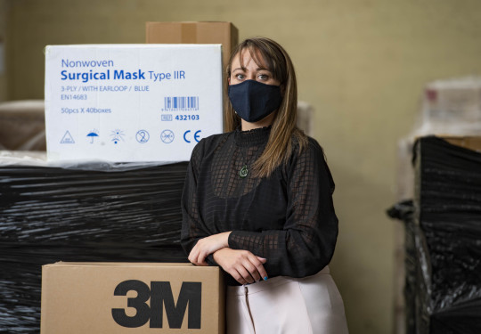 Tamara Hamiora is wearing a PPE mask, while leaning against a box of surgical masks and other PPE equipment.