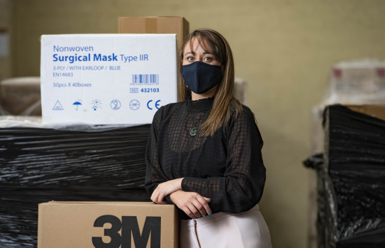 Tamara Hamiora is wearing a PPE mask, while leaning against a box of surgical masks and other PPE equipment.