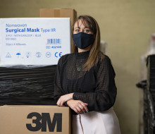 Tamara Hamiora is wearing a PPE mask, while leaning against a box of surgical masks and other PPE equipment.