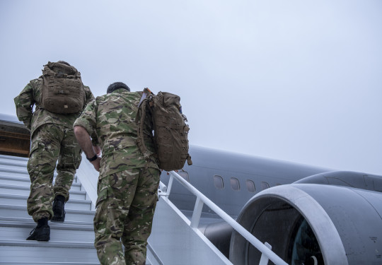 New Zealand Army personnel in uniform walk up the stars towards a Royal New Zealand Air Force Boeing aircraft. The sky is grey and it's a darker image. 