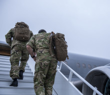 New Zealand Army personnel in uniform walk up the stars towards a Royal New Zealand Air Force Boeing aircraft. The sky is grey and it's a darker image.