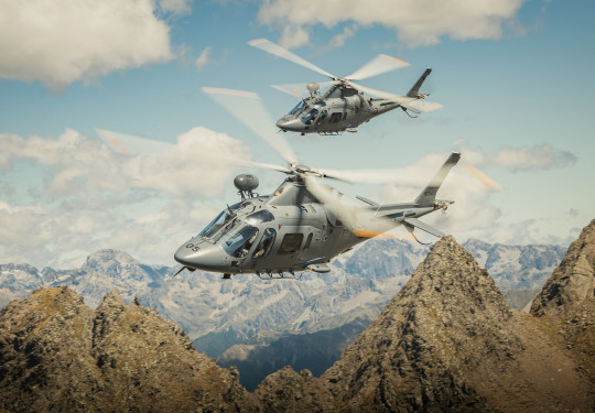 Two A109 helicopters fly over the mountain range. 