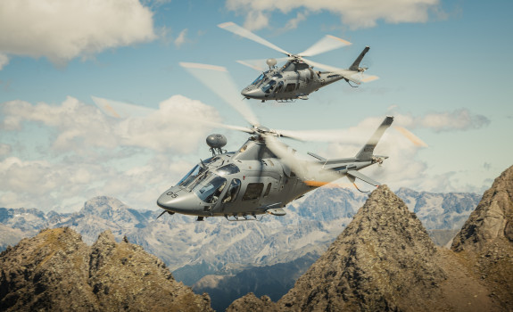 Two A109 helicopters fly over the mountain range.