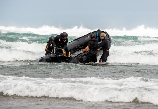 HMNZS Matataua's diving and hydrographic coxswains take a fully-crewed zodiac boat through the surf in the trecherous conditions of Auckland's Piha Beach.