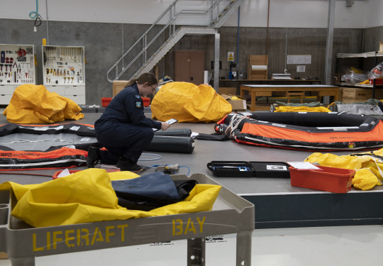 A Royal New Zealand Air Force Aviator working in the Liferaft Bay at Base Ohakea. There are liferafts and other equipment all over the floor. 