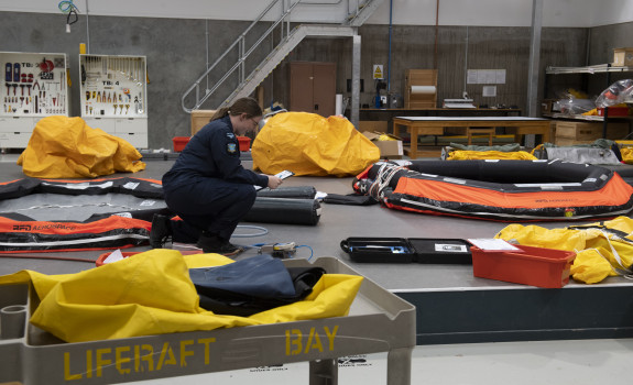 A Royal New Zealand Air Force Aviator working in the Liferaft Bay at Base Ohakea. There are liferafts and other equipment all over the floor. 