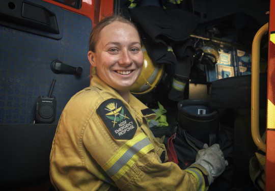 Sapper Danielle Brooks in a yellow firefighter jacket, smiling at the camera while standing beside a red firetruck