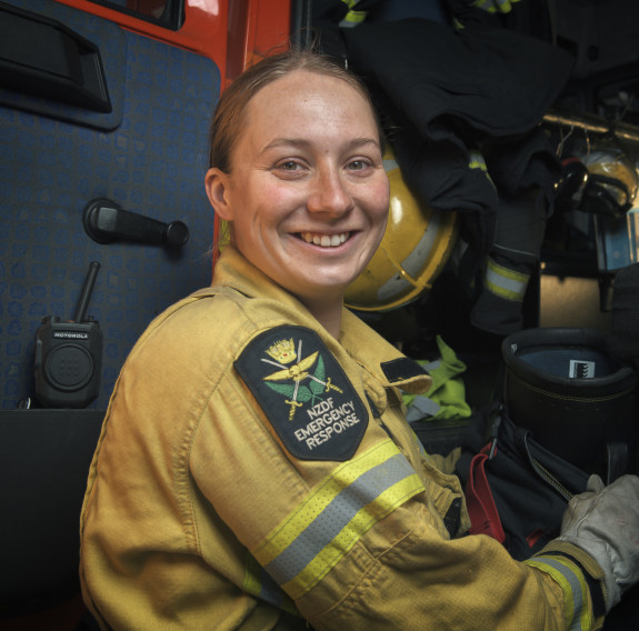 Sapper Danielle Brooks in a yellow firefighter jacket, smiling at the camera while standing beside a red firetruck