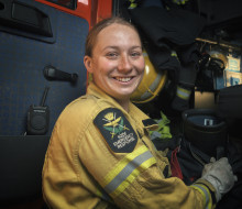 Sapper Danielle Brooks in a yellow firefighter jacket, smiling at the camera while standing beside a red firetruck