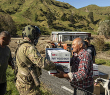 A Royal New Zealand Air Force NH90 helicopter crewman passes supplies to an Aropaoanui resident.