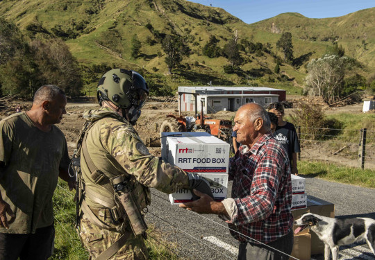 A Royal New Zealand Air Force NH90 helicopter crewman passes supplies to an Aropaoanui resident.
