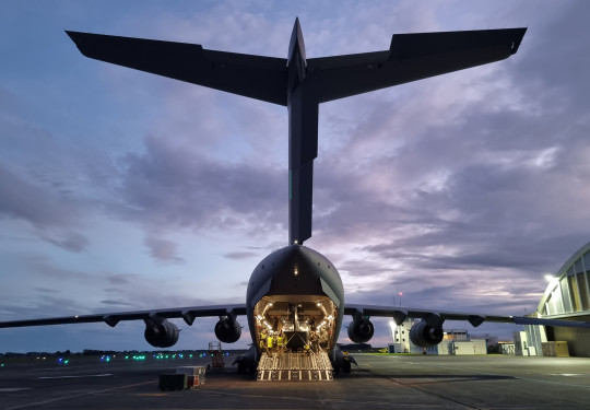 A NH-90 helicopter is loaded in the the rear of the RAAF C-17 at Base Ohakea. It's early in the morning and the clouds are glowing with the sunrise, the interior of the C-17 is lit by the interior lights.