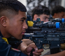 A sailor looks down the sight of gun on the Mobile Weapons Training System, with three others doing the same in the background.