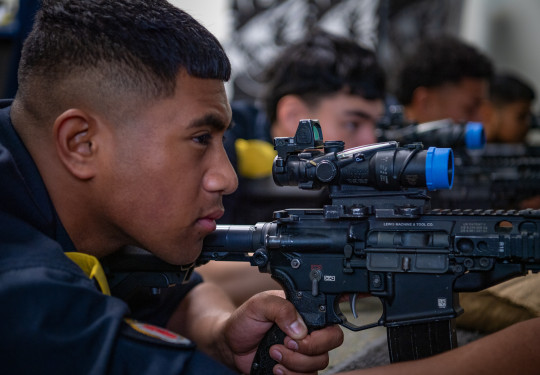 A sailor looks down the sight of gun on the Mobile Weapons Training System, with three others doing the same in the background.