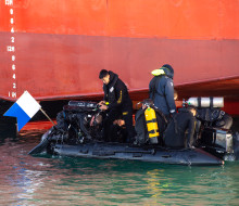 Divers, on a small boat prepare to dive in front of the the hull of a large ship.