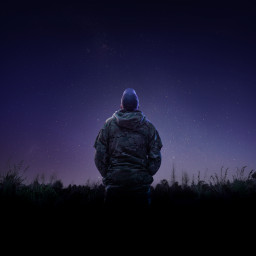 An aviator from the Royal New Zealand Air Force looks to the stars while wearing a camouflage jacket and a cap that has the letters 'RNZAF' on the back. 