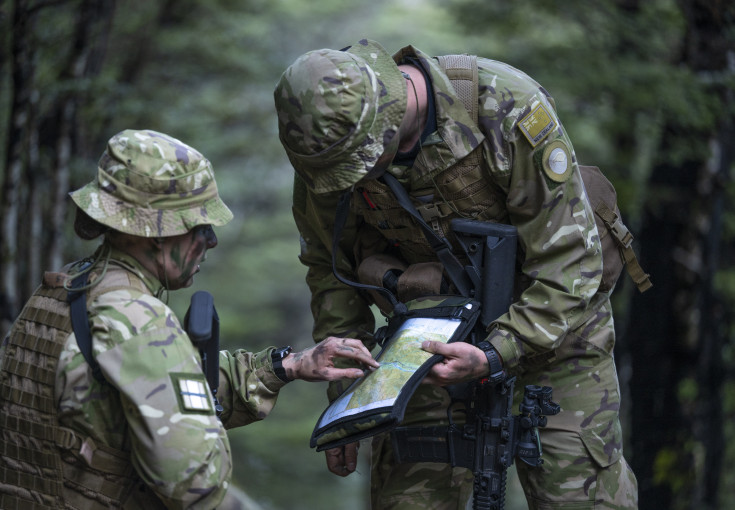 Two uniformed aviators look at a map in the bush. The image has a very green feel - green uniforms and green surrounding bush. One aviator is looking down and you can't see their face. The other, only the side of their face (they have camo on). The image 