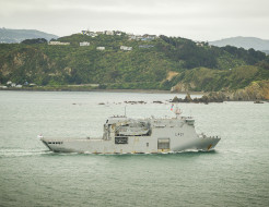 A grey Navy ship sails past Miramar Peninsular on the way into Wellington Harbour.