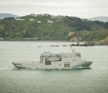 A grey Navy ship sails past Miramar Peninsular on the way into Wellington Harbour.