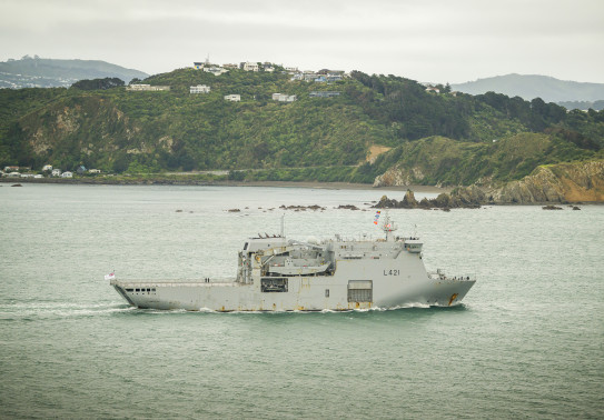 A grey Navy ship sails past Miramar Peninsular on the way into Wellington Harbour.