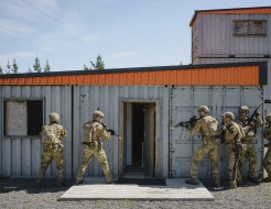 Soldiers prepare to enter a building made of containers.