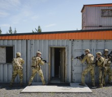 Soldiers prepare to enter a building made of containers.