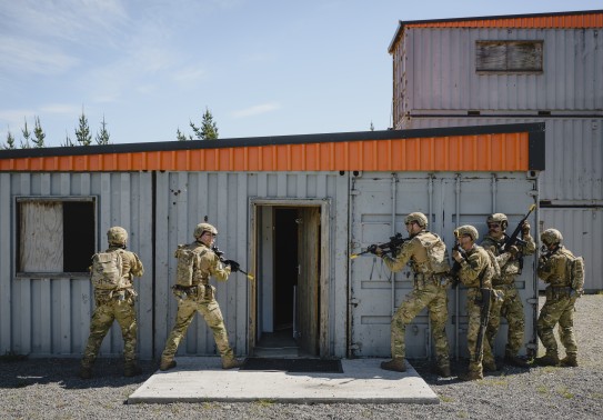 Soldiers prepare to enter a building made of containers.
