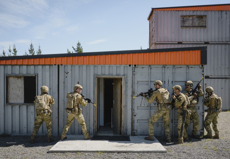 Soldiers prepare to enter a building made of containers.