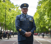 Warrant Officer Paul Chadwick in Air Force uniform standing on the streets of London framed by green trees of Summer.