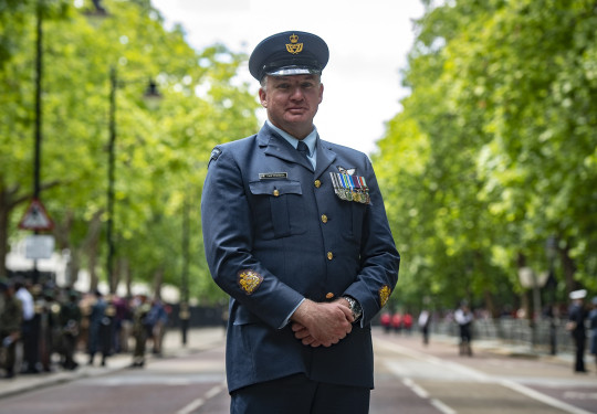 Warrant Officer Paul Chadwick in Air Force uniform standing on the streets of London framed by green trees of Summer.