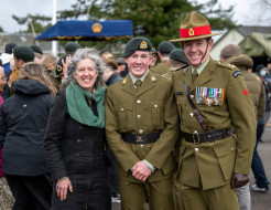  Proud Mum in a jacket and green scarf on the left, while the son and Dad (on the right) are in Army uniforms on the parade ground in front of other families and soldiers.