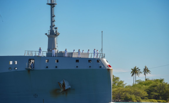 HMNZS Aotearoa sailing into Hawaii's Pearl Harbour on a sunny day with palm trees featuring in the background.