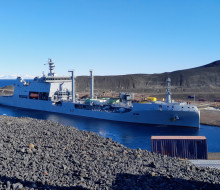HMNZS Aotearoa arriving at McMurdo Station in Antartica behind a metal sign that reads 'McMurdo Station Antartica.'