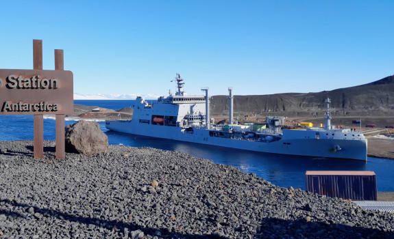 HMNZS Aotearoa arriving at McMurdo Station in Antartica behind a metal sign that reads 'McMurdo Station Antartica.'