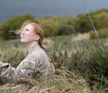 A soldier looks up while setting up a radio antenna mast in the field.
