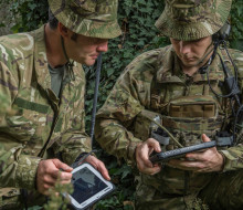 Soldiers in the field with tactical communications equipment look at tablets.