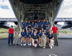 Group photo of students in blue t-shirts in the rear ramp of a Hercules aircraft.