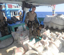 Sailors on French Frigate FS Floreal stands with a dog surrounded by illicit drugs seized.
