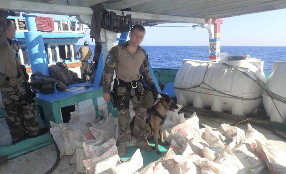 Sailors on French Frigate FS Floreal stands with a dog surrounded by illicit drugs seized.