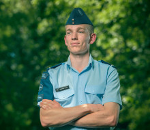 Cadet Warrant Officer Hamish Cook stands smiling, looking away form the camera with greenery in the background.